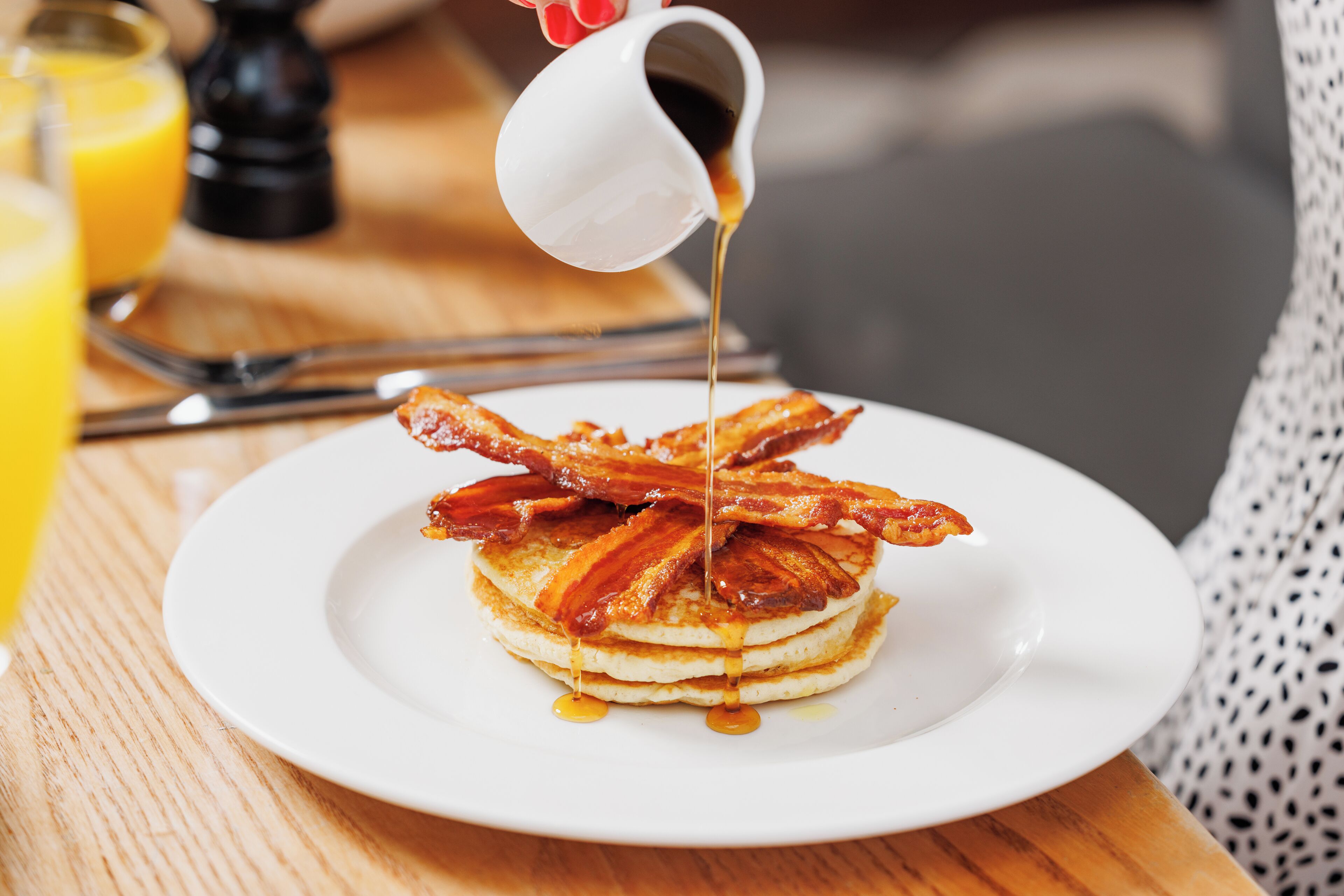 A plate of pancakes with syrup and bacon on a wooden table.