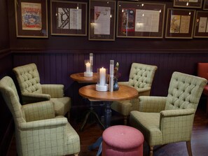 A room with four upholstered chairs, two round tables with candles, and framed documents on the wall. - The Richard Onslow (Cranleigh)