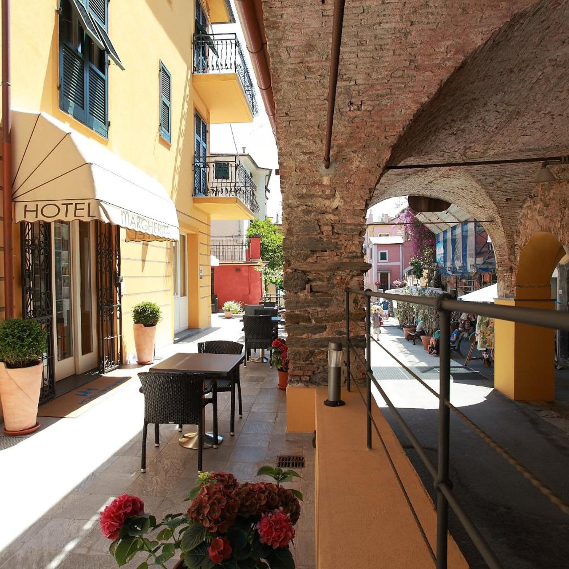 Un cortile alberghiero con posti a sedere all'aperto, un arco in pietra e vista sulla strada.