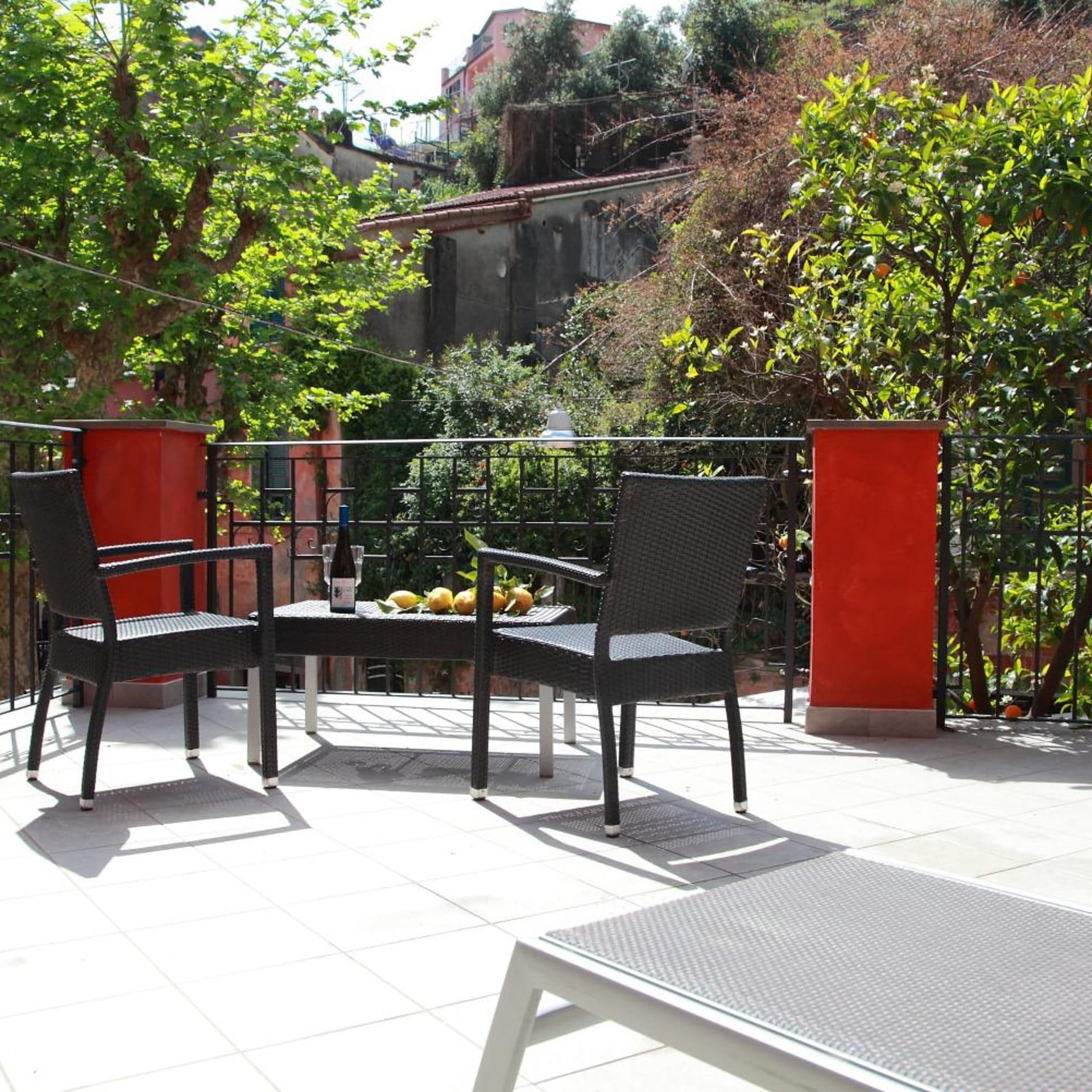 Zona salotto esterna con tavolo e sedie, immersa nel verde e delimitata da un muro rosso.