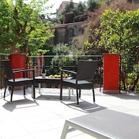 An outdoor seating area with a table and chairs, surrounded by greenery and a red wall.