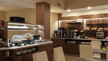 Un'area ristorazione moderna in un hotel, con un buffet, macchine da caffè e un lungo tavolo apparecchiato per gli ospiti.