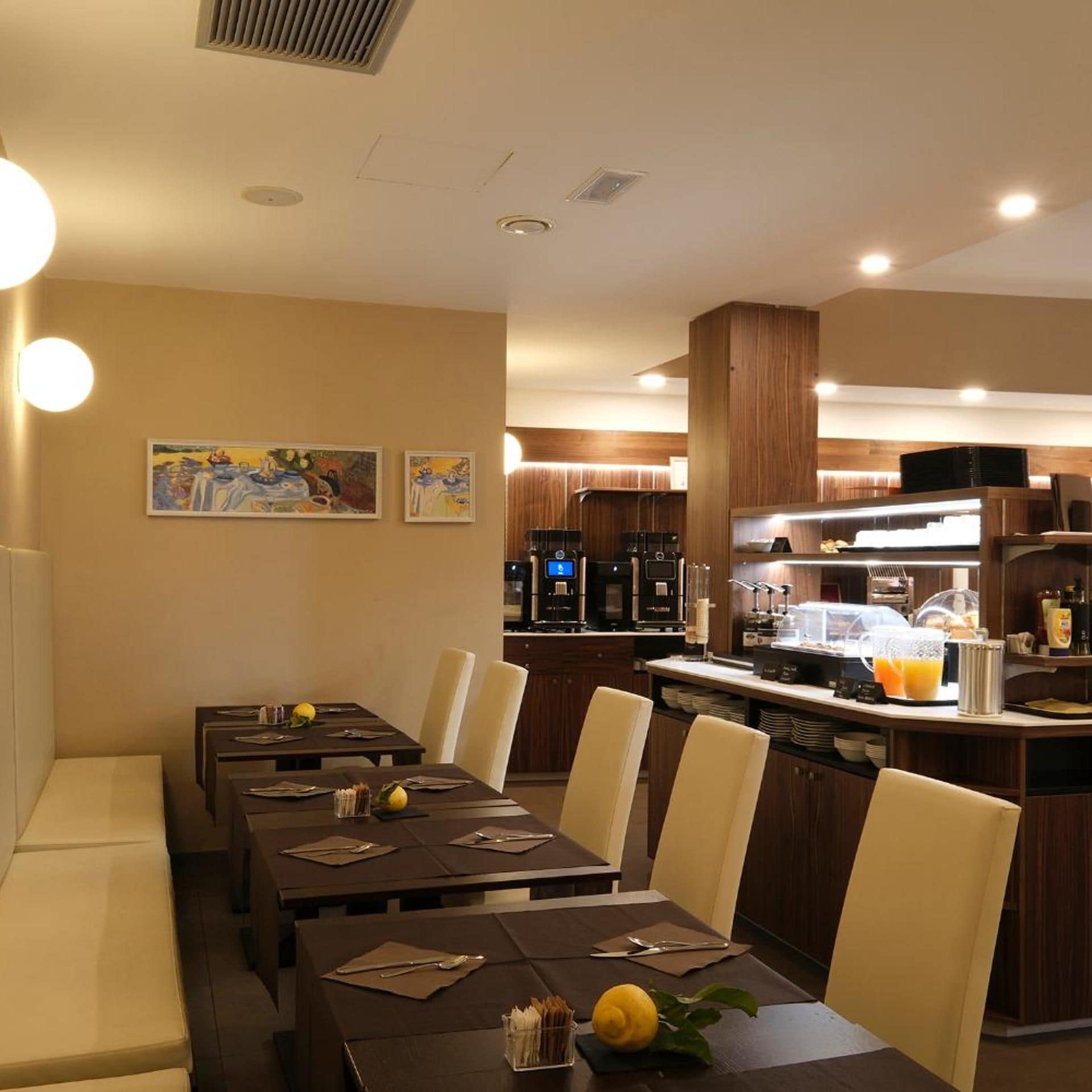 Un ristorante con diversi tavoli, sedie e un'area cucina con macchine per caffè e un espositore di frutta.