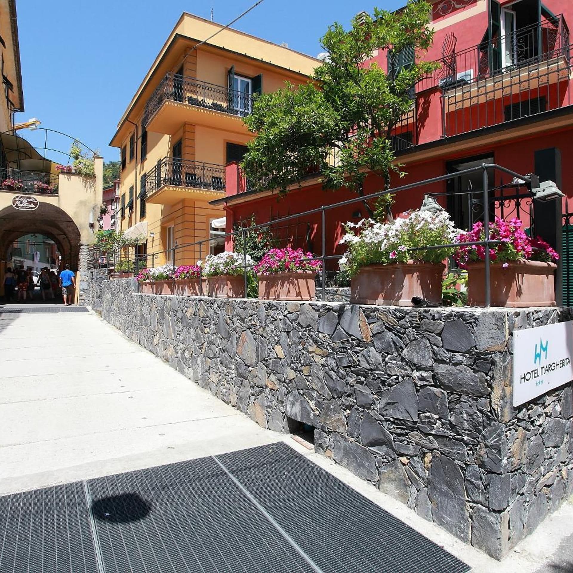 Un muro in pietra, un cartello di un albergo, un marciapiede lastricato e edifici con balconi.