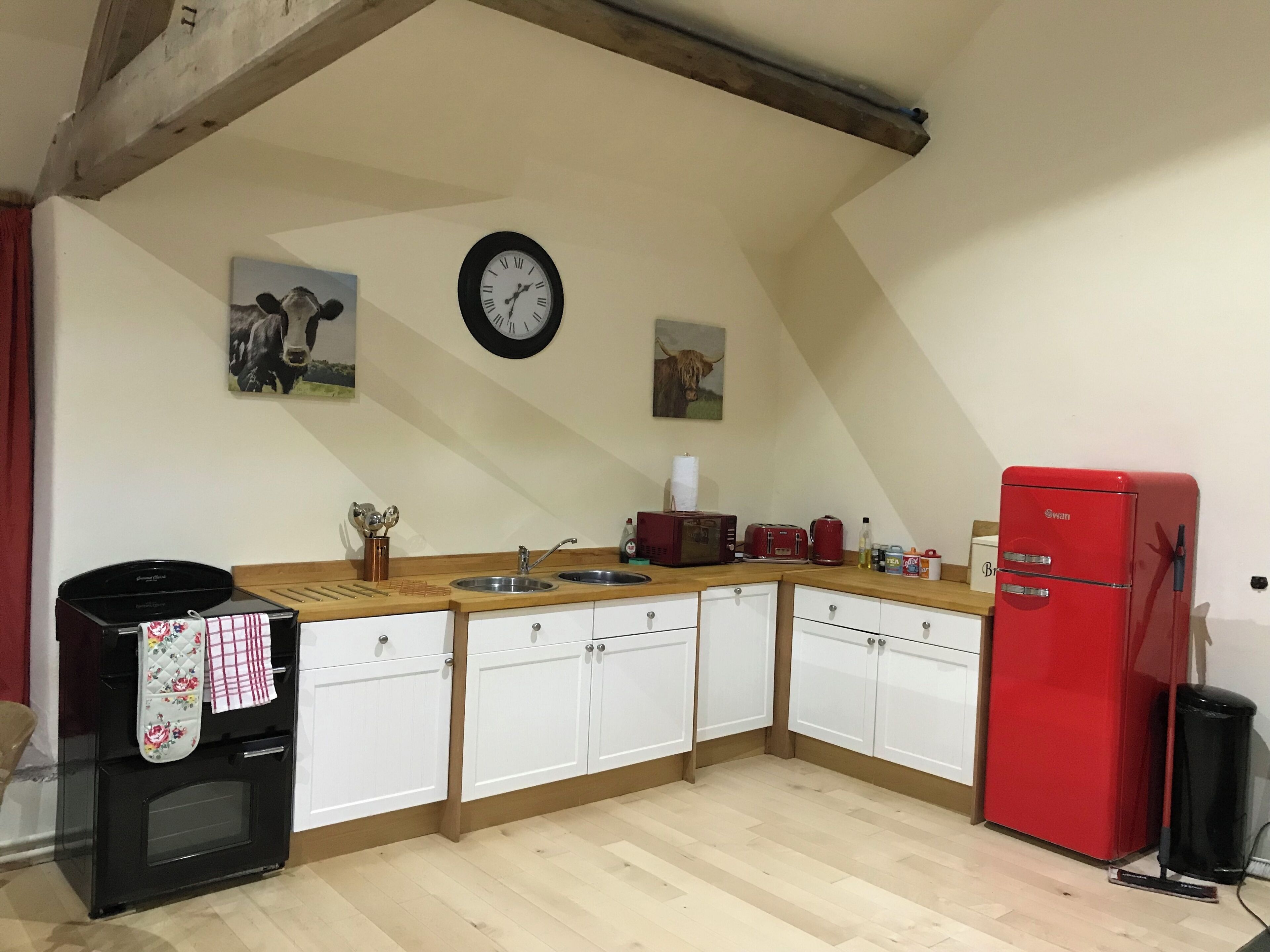 A kitchen with white cabinets, a wooden countertop, a red refrigerator, a microwave, a toaster, and a clock on the wall.