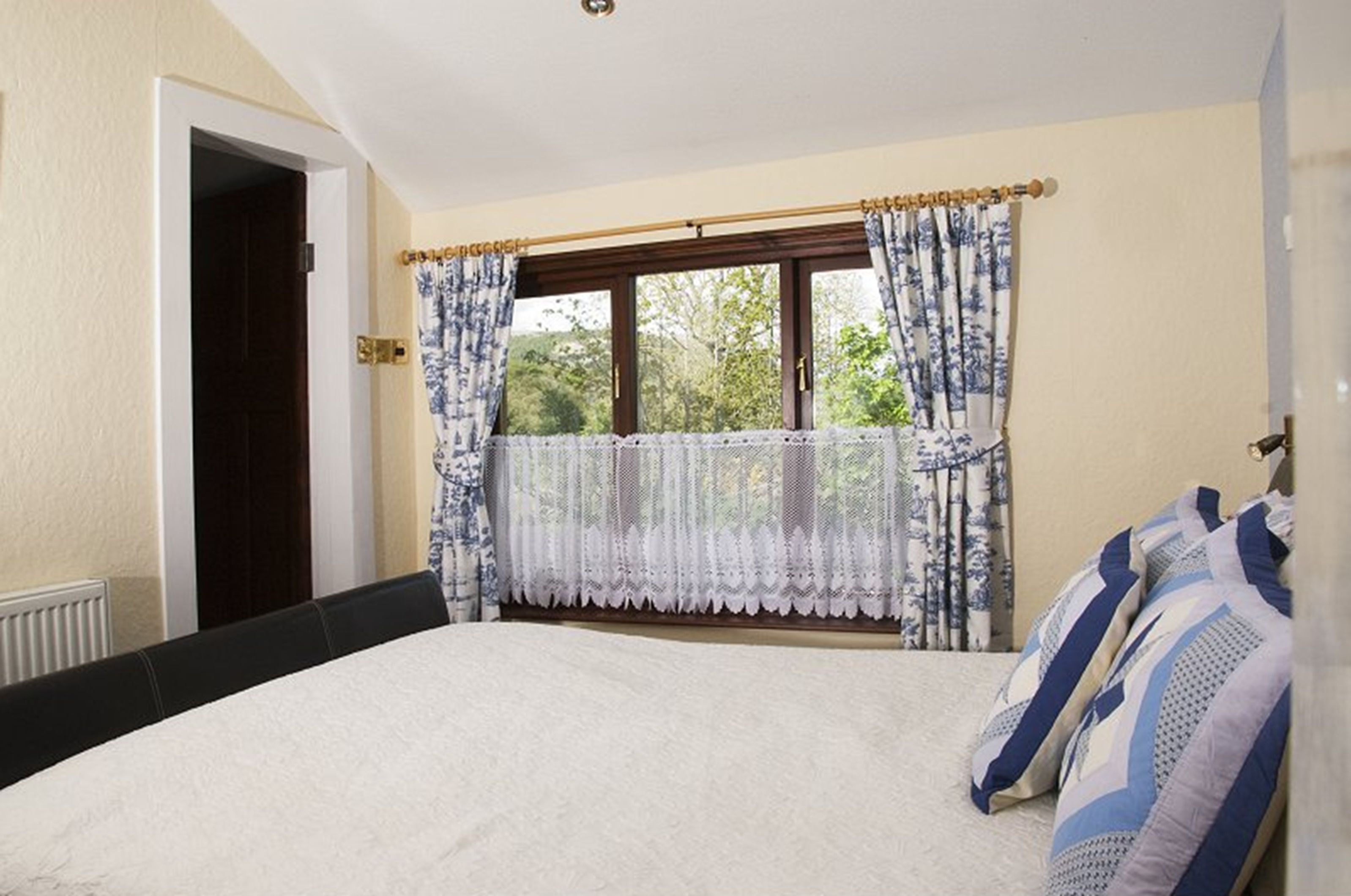 A bedroom with a bed, a window with curtains, a radiator, and a door.