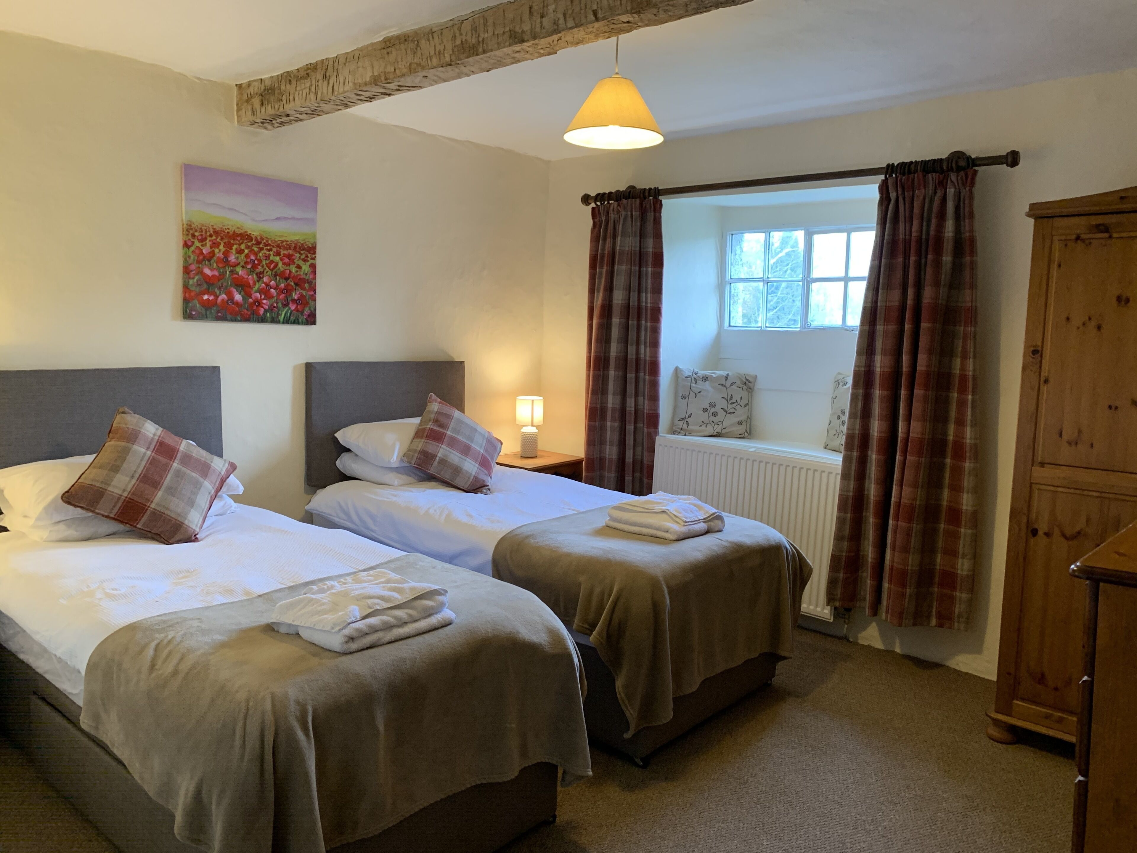 Une chambre d’hôtel avec deux lits, une fenêtre avec des rideaux, un radiateur et une armoire en bois.