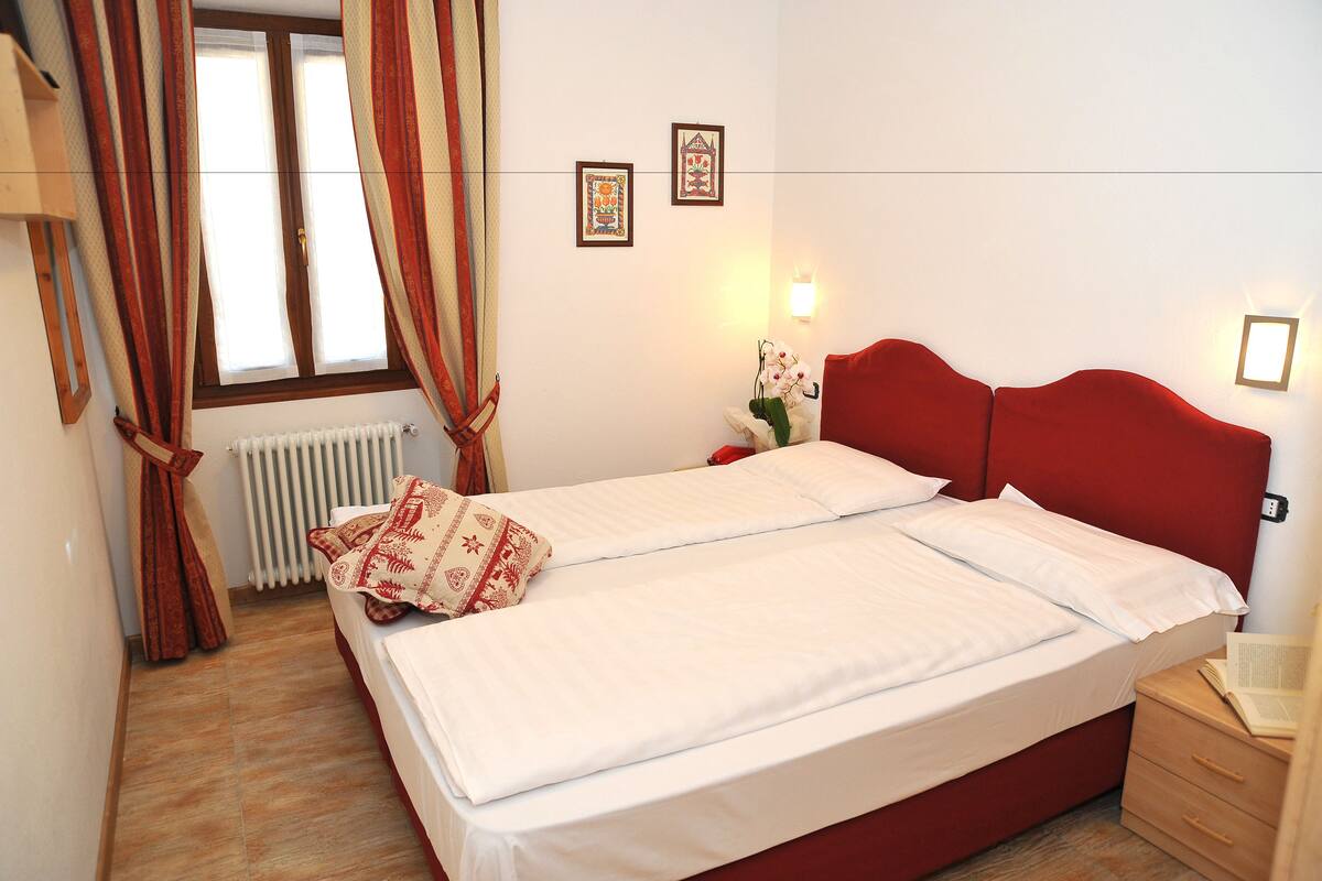 A double bed with white linens, a red headboard, and a nightstand with a lamp.