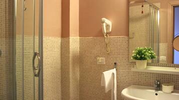 Un bagno con una cabina doccia in vetro, un lavandino bianco, un asciugamano appeso al muro e una pianta in vaso.