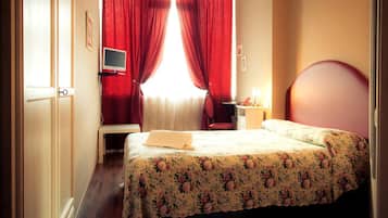 Una camera d'albergo con un letto, una scrivania, una sedia, una televisione e tende rosse.