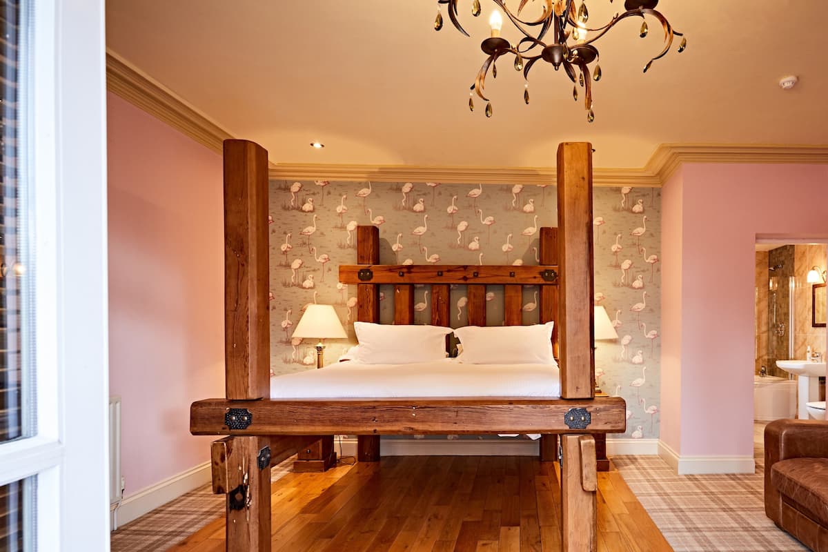 A bedroom with a wooden four-poster bed, a chandelier, and a bathroom visible to the right.