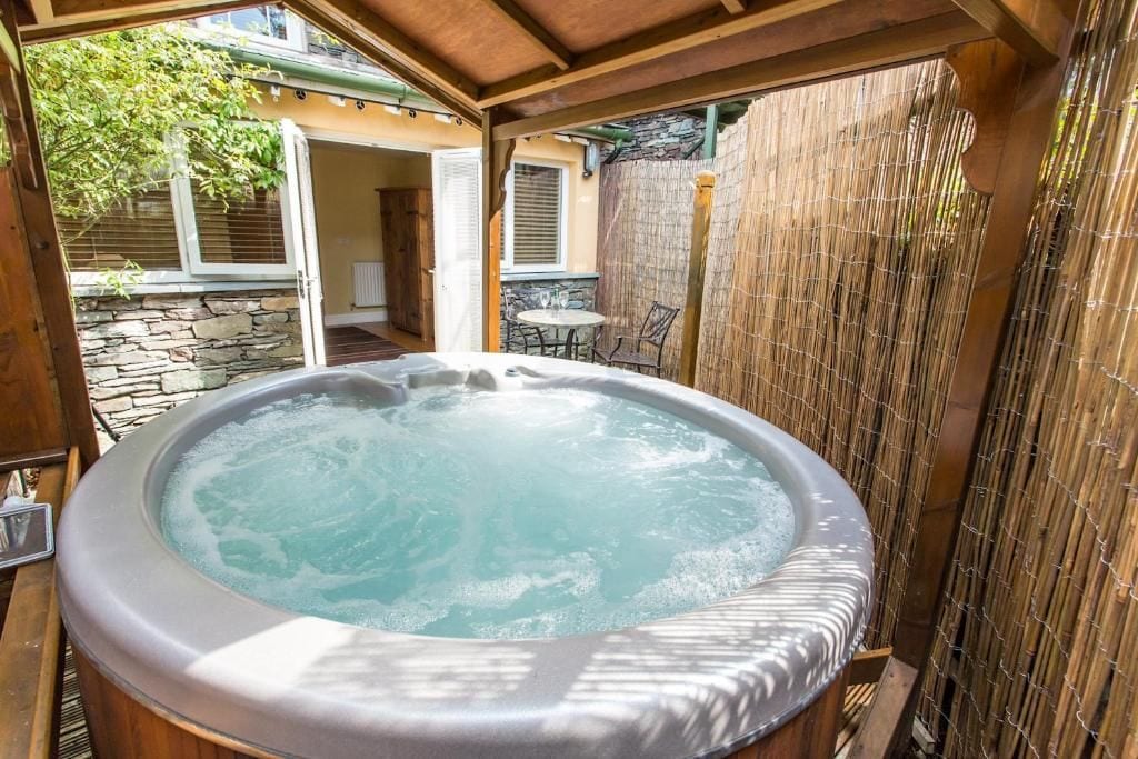 Un jacuzzi en un entorno exterior con una valla de bambú y un muro de piedra al fondo.