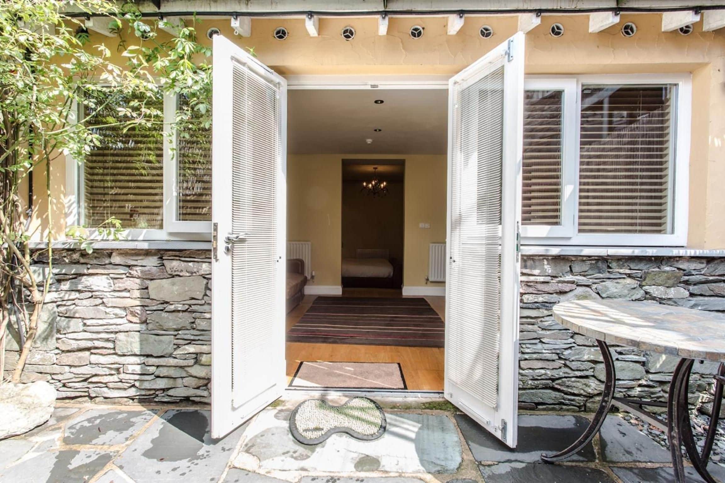 A hotel entrance with open doors leading to a bedroom with a bed and a chandelier.