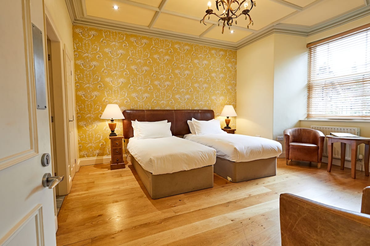 A hotel room with two beds, a desk, a chair, and a window with blinds.