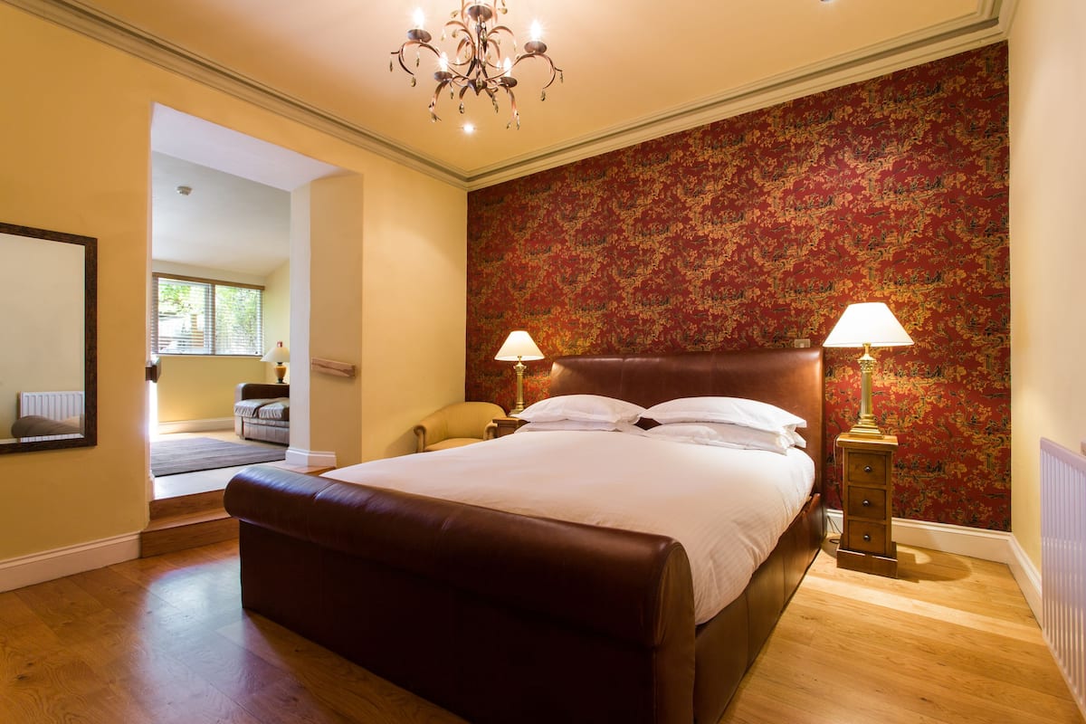 A bedroom with a large bed, two bedside lamps, a chandelier, and a patterned wallpaper.