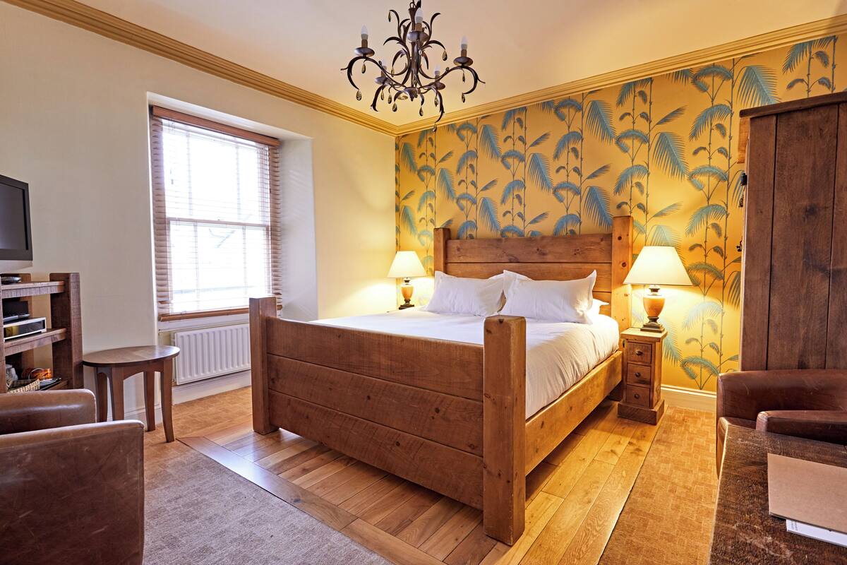 A wooden bed with two bedside tables, a chandelier, and a window with blinds.