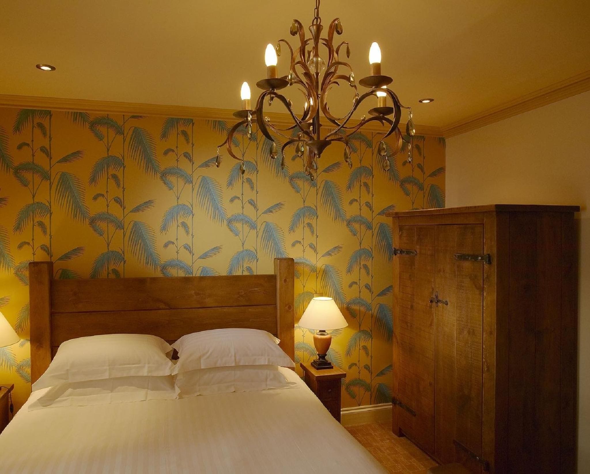 A bedroom with a wooden bed, a chandelier, a nightstand with a lamp, and a wardrobe.