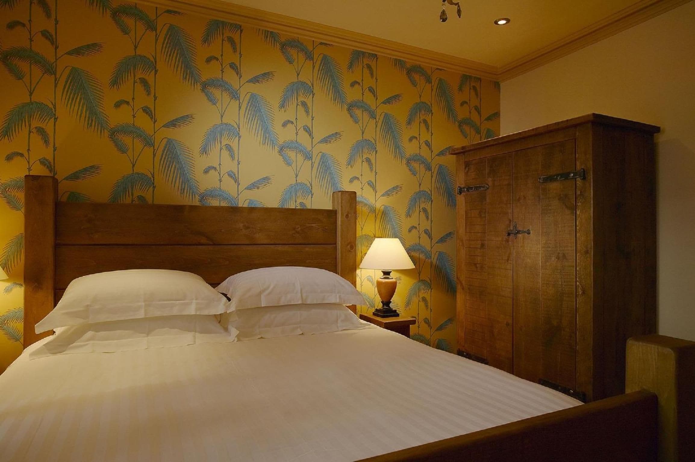 A hotel room with a bed, a nightstand with a lamp, and a wooden wardrobe.