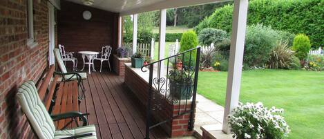A covered patio with wooden flooring, a brick wall, and a view of a well-maintained garden.