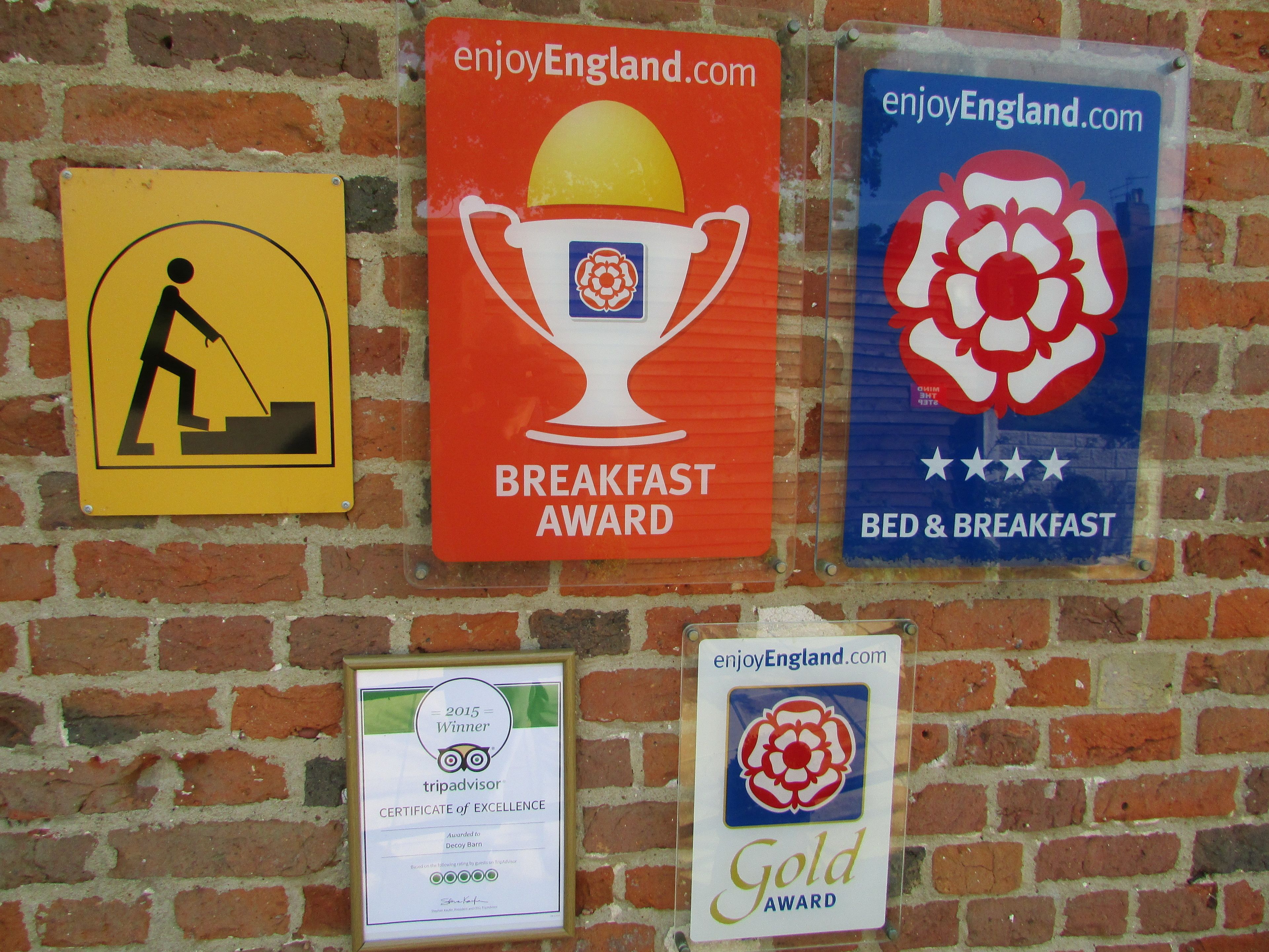 A wall with multiple signs, including a yellow sign with a person digging, a red sign with a trophy labeled 'Breakfast Award', and a blue sign with a flower and stars labeled 'Bed & Breakfast'.