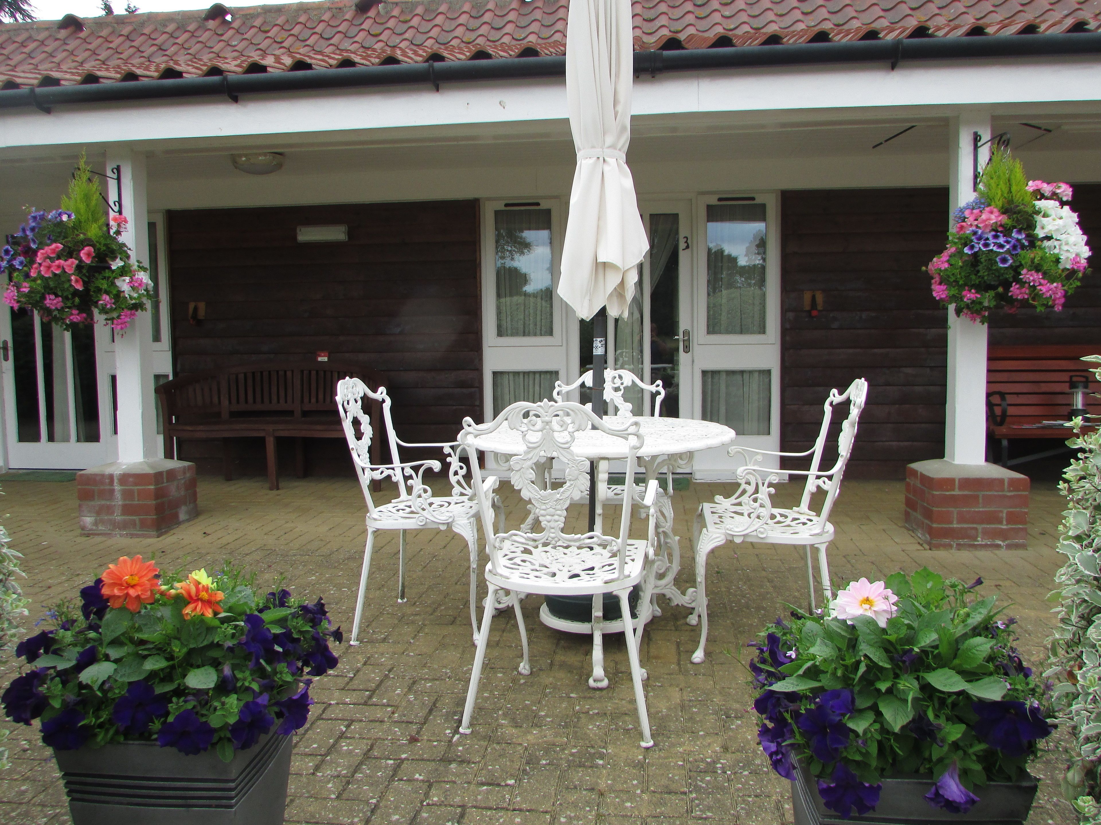 Eine Terrasse mit einem weißen Metalltisch und Stühlen, umgeben von Blumenkästen.
