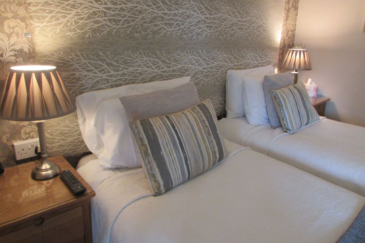 Ein Hotelzimmer mit zwei Betten, einem Nachttisch mit Lampe und einer Fernbedienung.