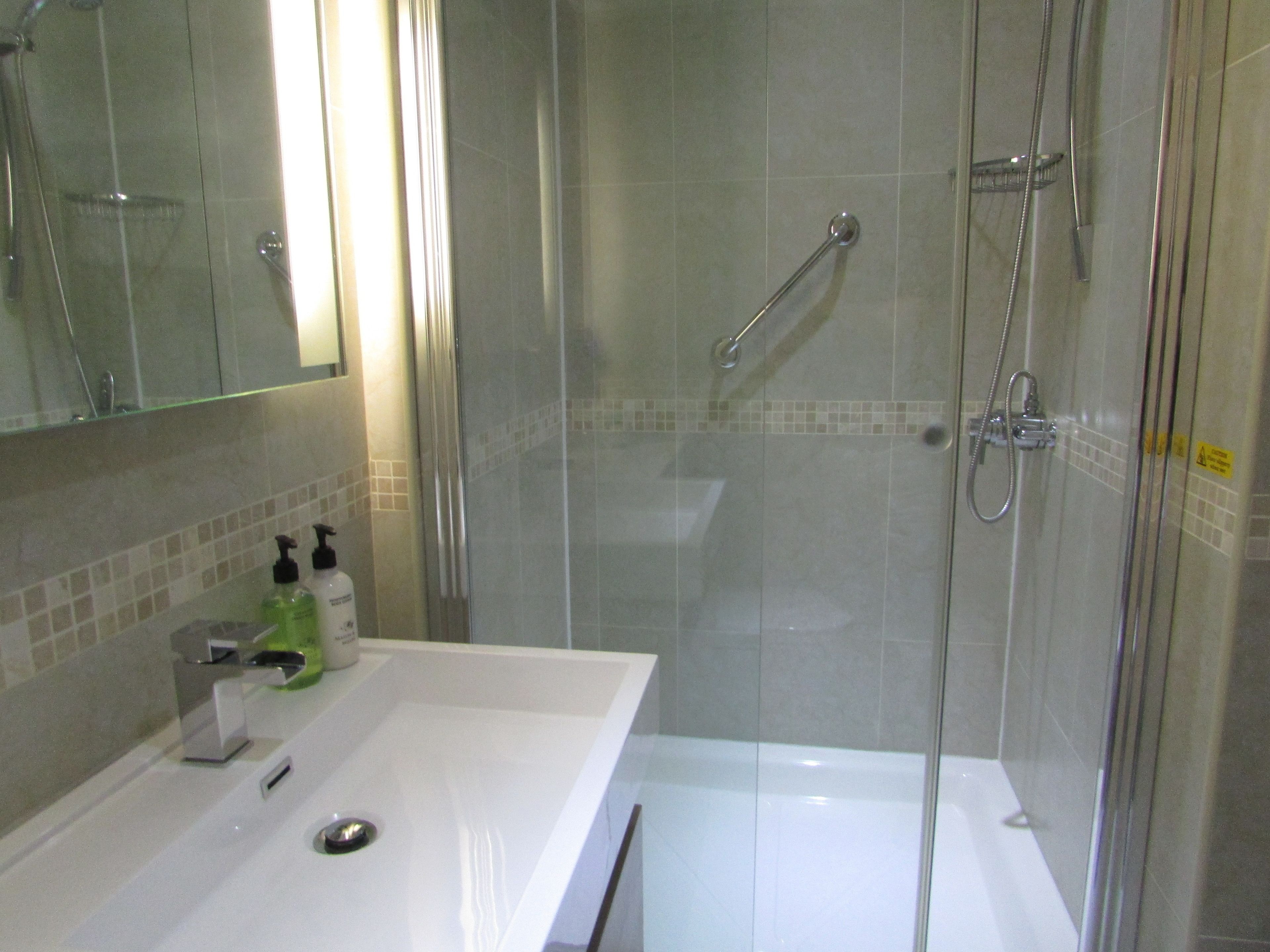 A bathroom with a glass-enclosed shower, a white sink with a mirror, and toiletries on the counter.