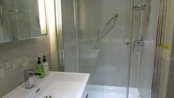 A bathroom with a glass-enclosed shower, a white sink with a mirror, and toiletries on the counter.
