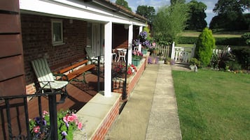 Eine überdachte Veranda mit Sitzgelegenheiten, eine Ziegelwand und ein Garten mit Blumen und Rasen.