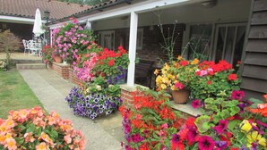 A covered patio area with a brick wall, outdoor furniture, and a variety of potted flowers. - Decoy Barn (Great Yarmouth)