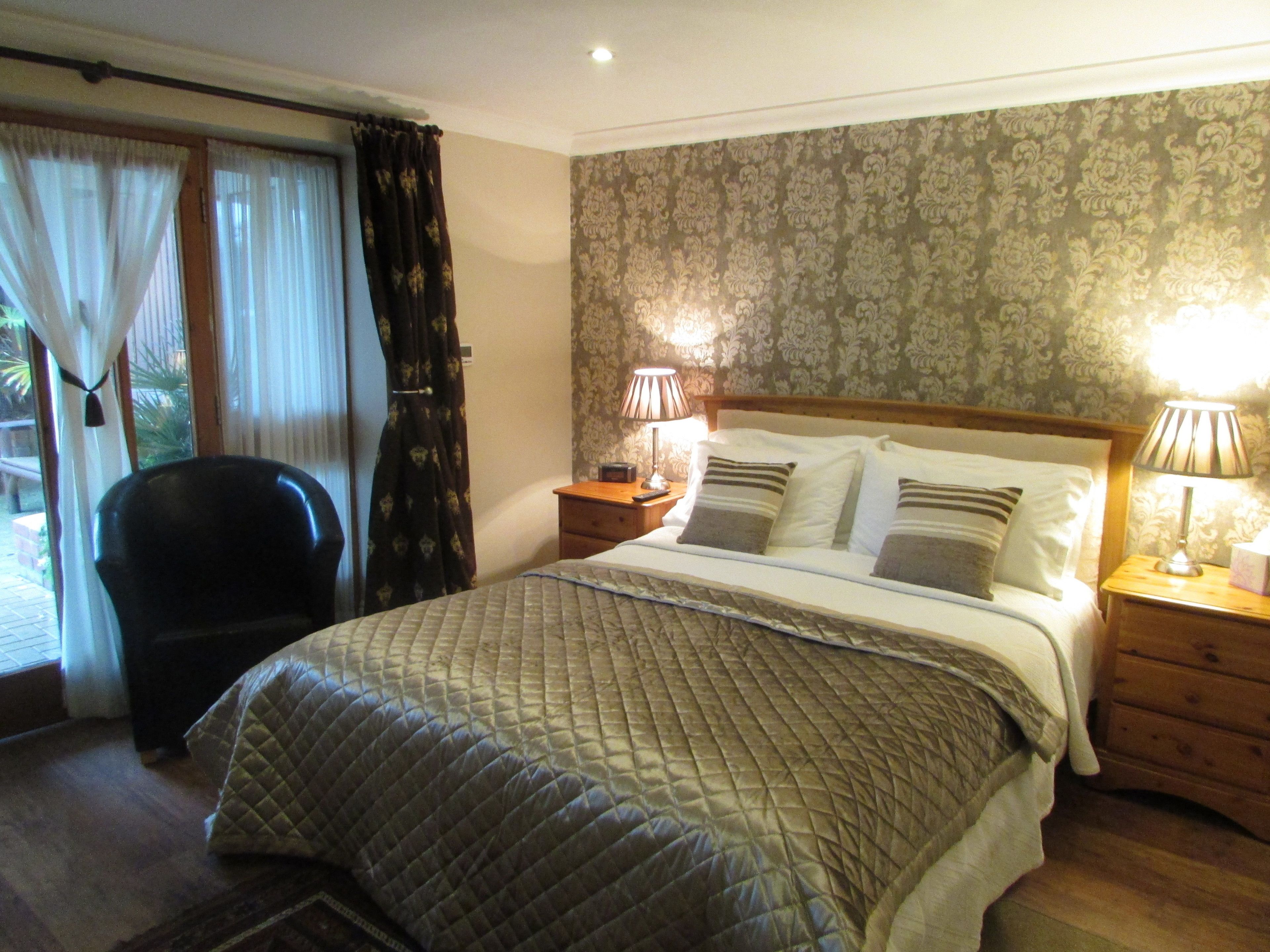 Une chambre d’hôtel avec un lit, deux tables de chevet avec des lampes, une chaise et une vue sur l’extérieur à travers une fenêtre avec des rideaux.