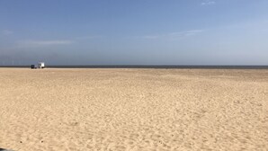 Une vaste plage de sable avec une petite construction blanche visible au loin.
