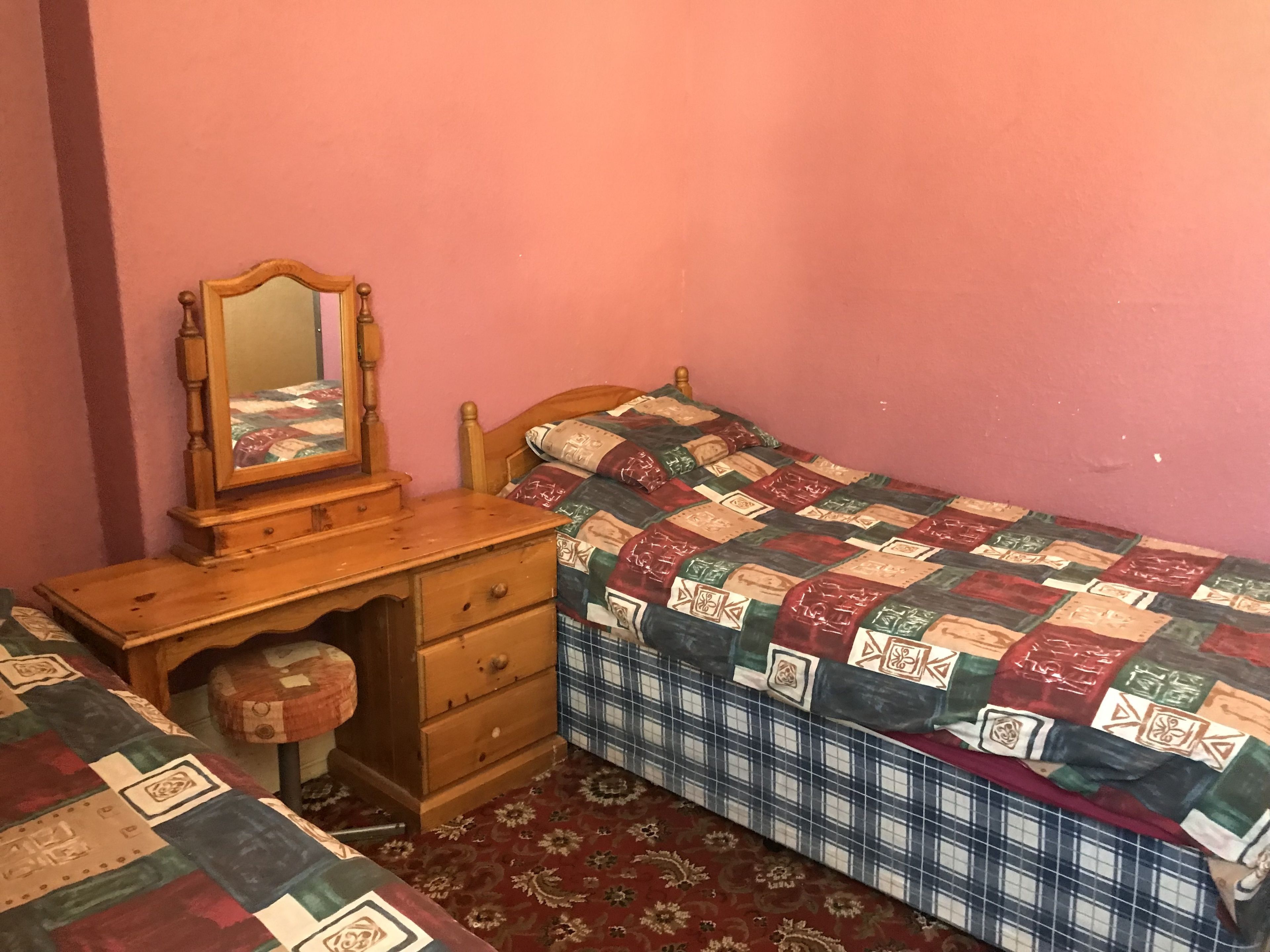 A bedroom with a wooden dresser, a bed with a quilt, and a mirror.