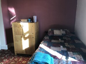Quarto com um armário de madeira, uma cama com colcha estampada e um tapete vermelho.