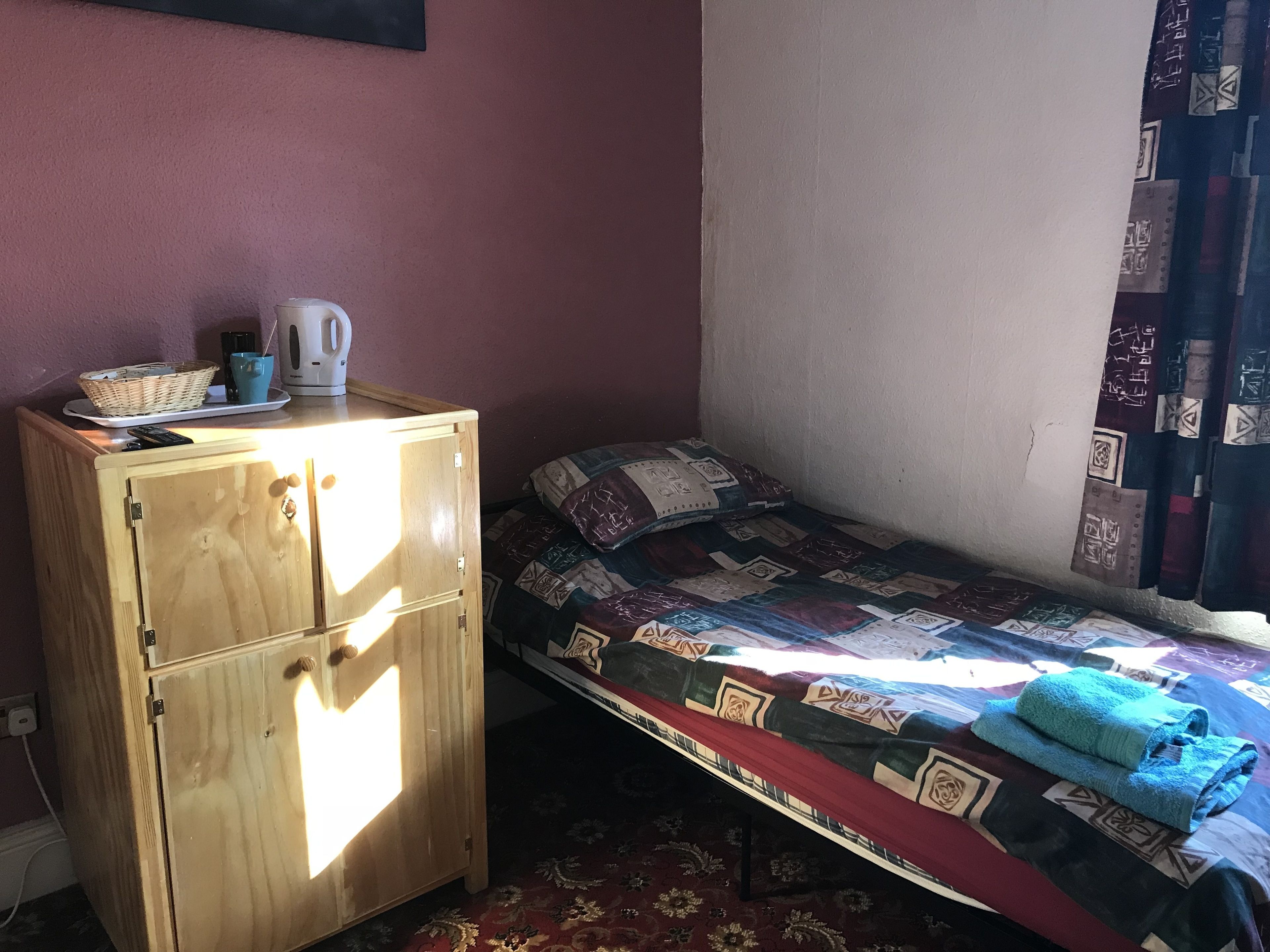 Un dormitorio pequeño con un armario de madera, una cama con colcha estampada y una ventana con cortinas.