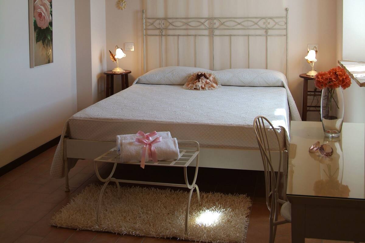 A bedroom with a bed, bedside tables, a chair, a small table, and a decorative vase.