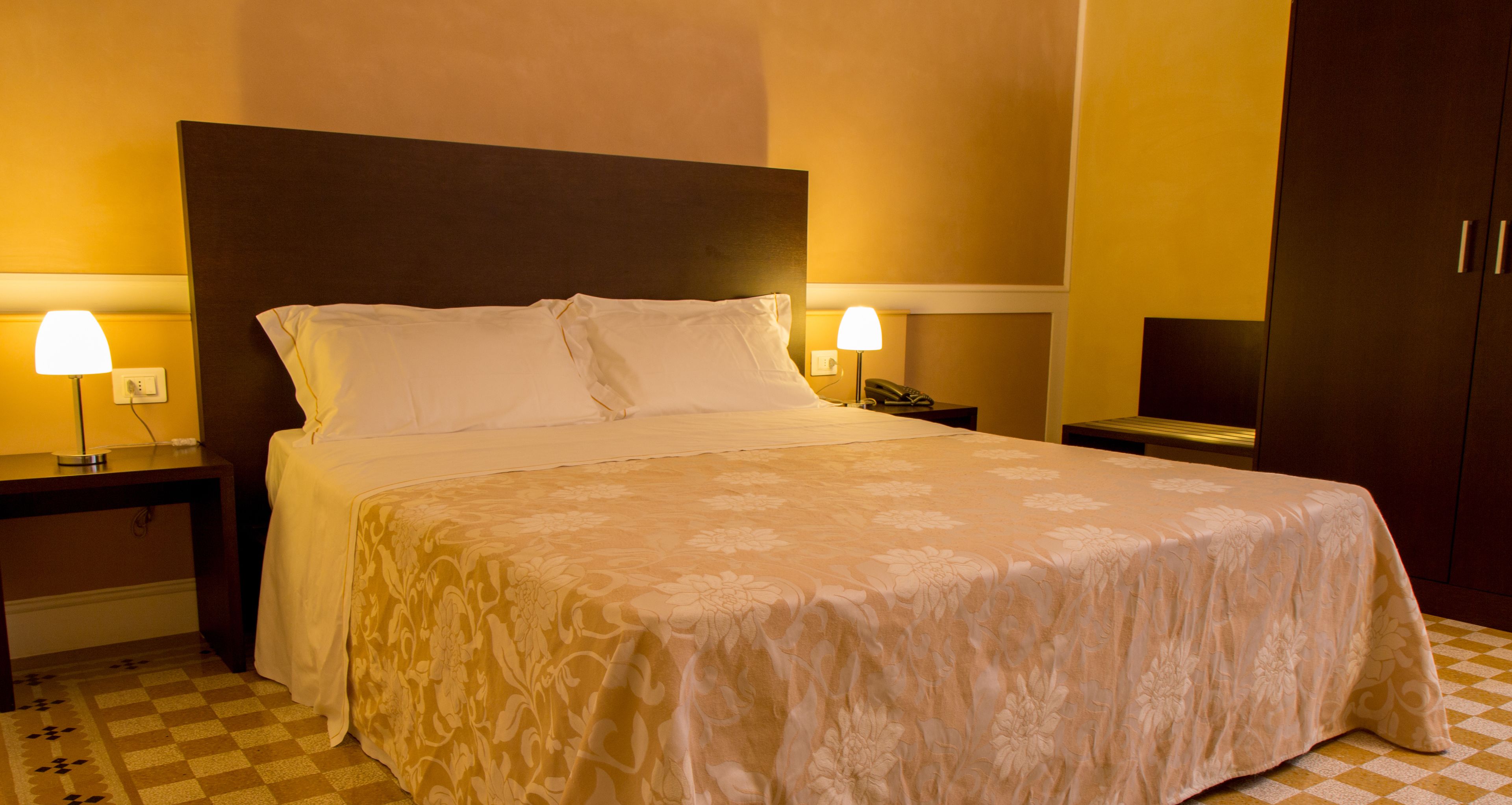 Habitación de hotel con una cama grande, dos mesitas de noche con lámparas, un armario y un suelo a cuadros.