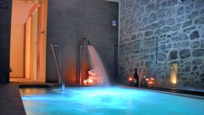 A hot tub with a stone wall backdrop, a metal faucet, and candles. - Relais Del Borgo Hotel e Spa (Staffolo)