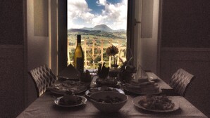 A dining table set with plates, a bowl, and a bottle, with a scenic view of mountains and a vineyard through a window. - Relais Del Borgo Hotel e Spa (Staffolo)