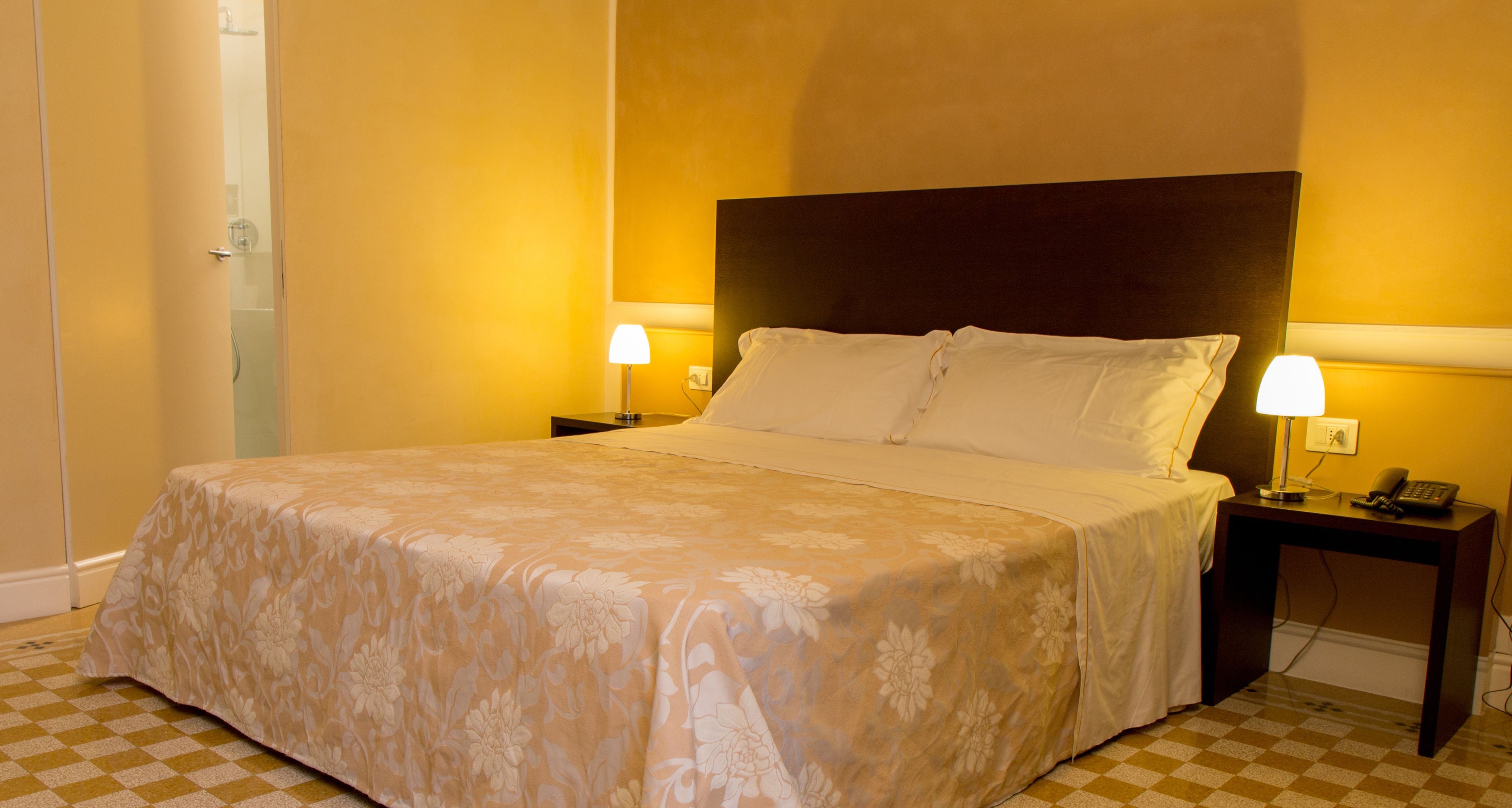 Una habitación de hotel con una cama grande, dos mesitas de noche con lámparas y un suelo a cuadros.