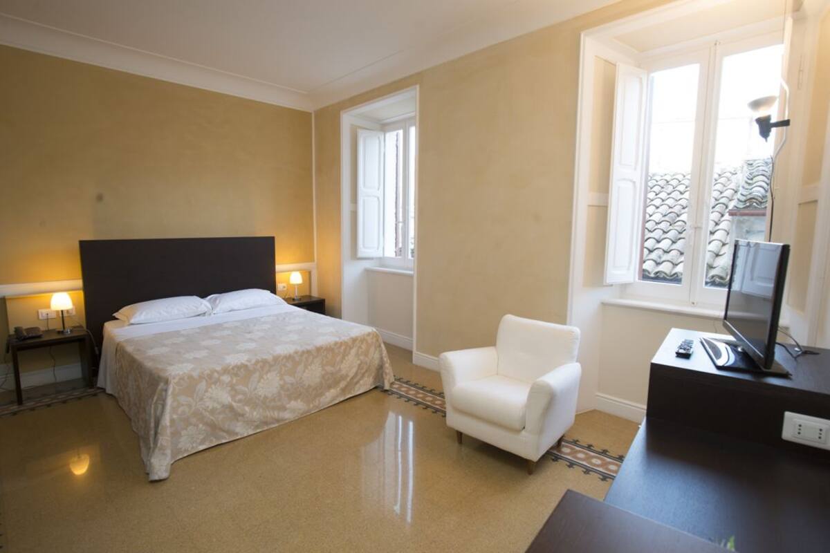 Een hotelkamer met een bed, een stoel, een bureau met een televisie en een raam met uitzicht op het exterieur.
