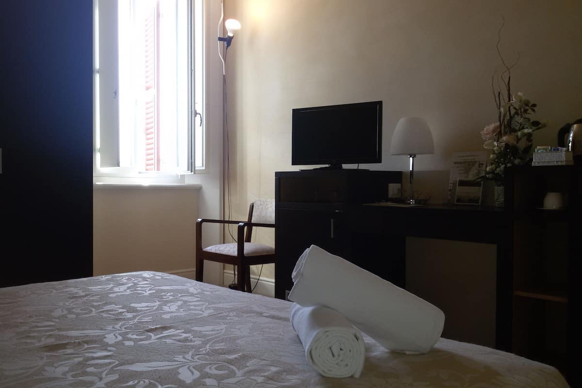 Een hotelkamer met een bed, een bureau, een stoel, een televisie en een raam met jaloezieën.