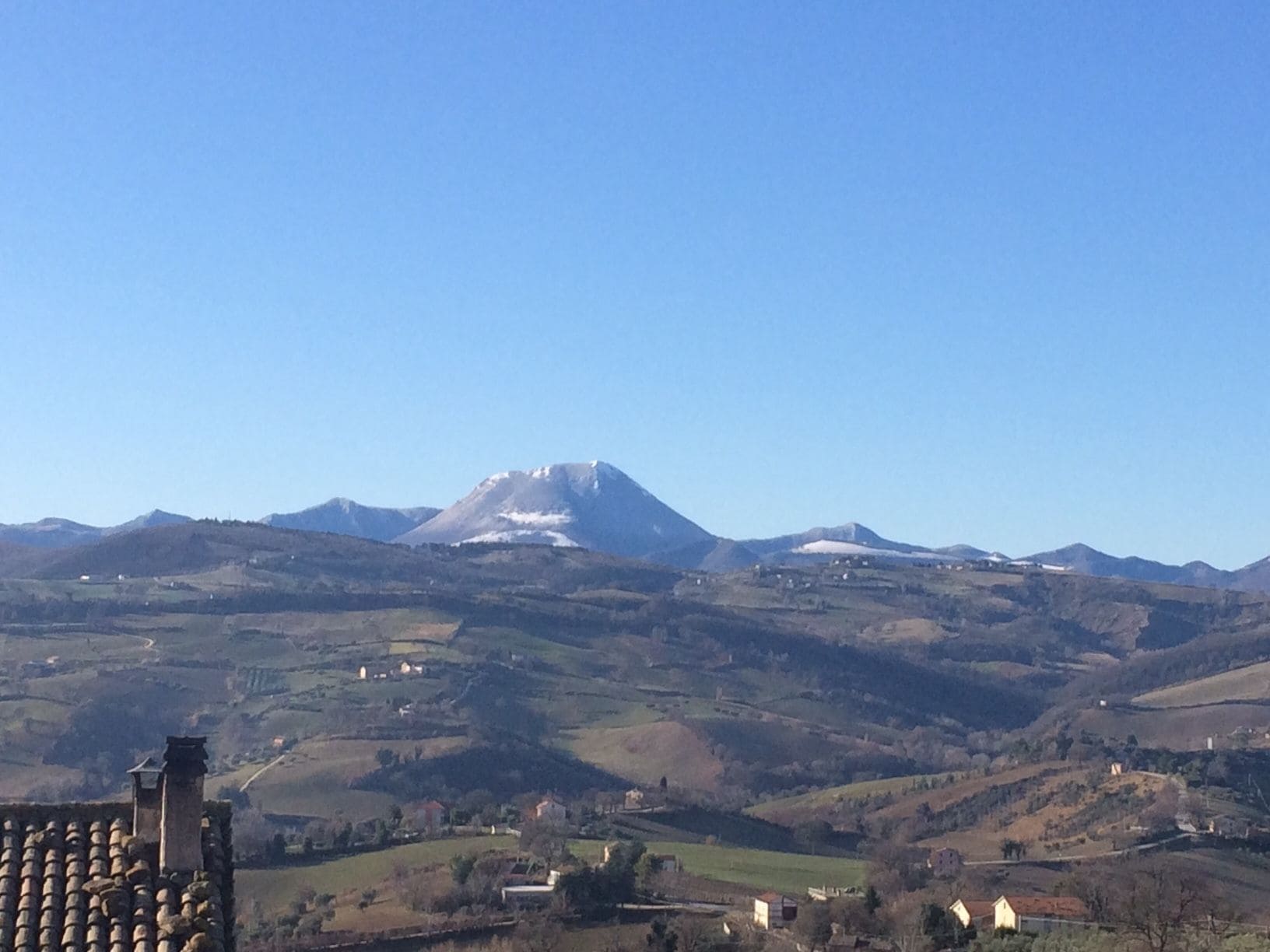 Un paisaje montañoso con un pico destacado, colinas onduladas y edificios dispersos.