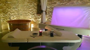 Ein Bereich für Spa-Behandlungen mit einer Holzwanne, einer Massageliege, einem weißen Handtuch und einem Massagesessel.