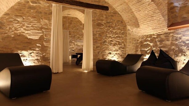 A stone-walled room with modern black sofas and a wooden beam ceiling. - Relais Del Borgo Hotel e Spa (Staffolo)