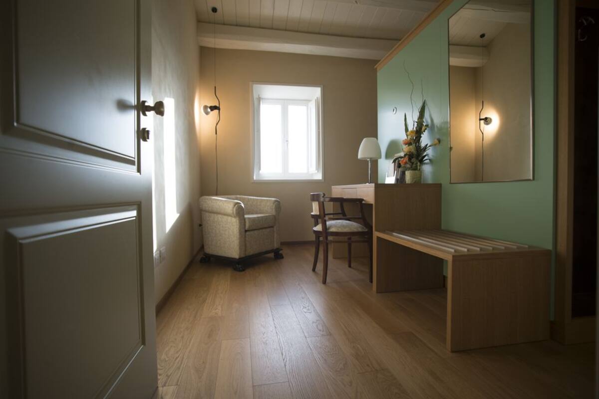 Een kamer met houten vloer, een stoel, een bureau, een spiegel en een raam.