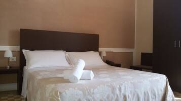Un lit bien fait, avec des draps blancs et une couvre-lit à motifs floraux, deux oreillers blancs et une serviette enroulée posée sur le lit.