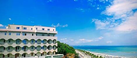 A hotel with a modern design, located near a beach with a clear sky.