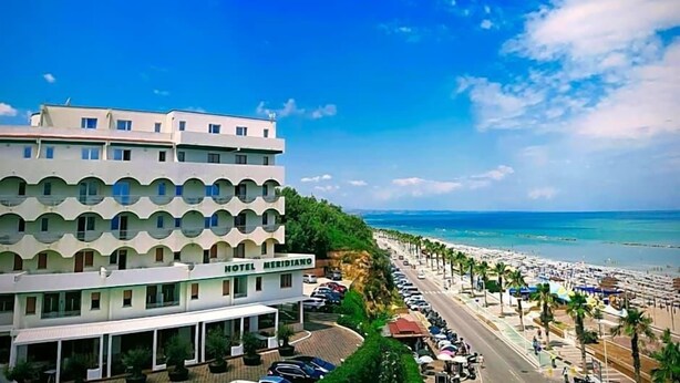 A hotel with a modern design, located near a beach with a clear sky.