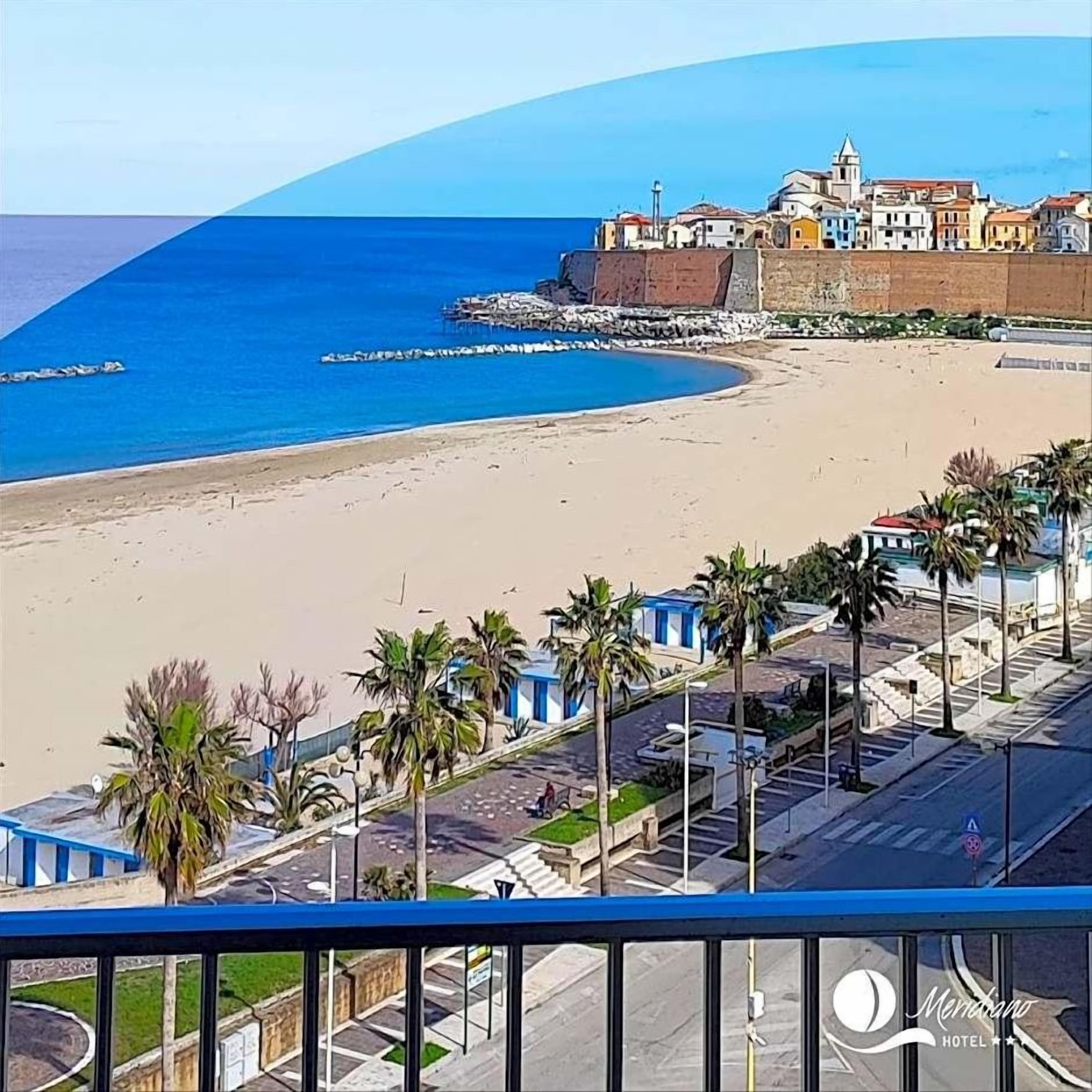 A coastal hotel with a beach view, palm trees, and a clear blue sky.